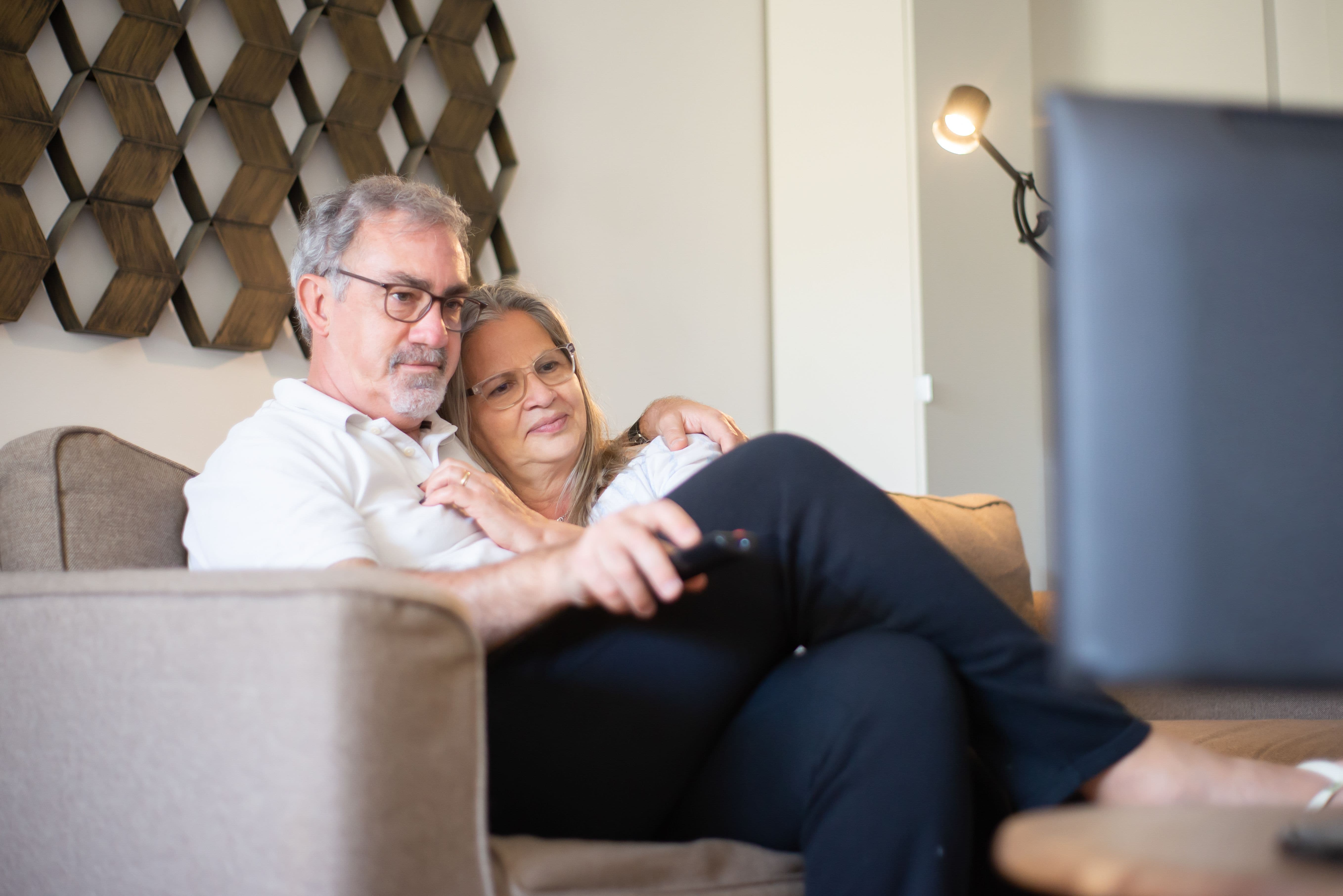 Older couple sitting on a couch using a TV remote at home